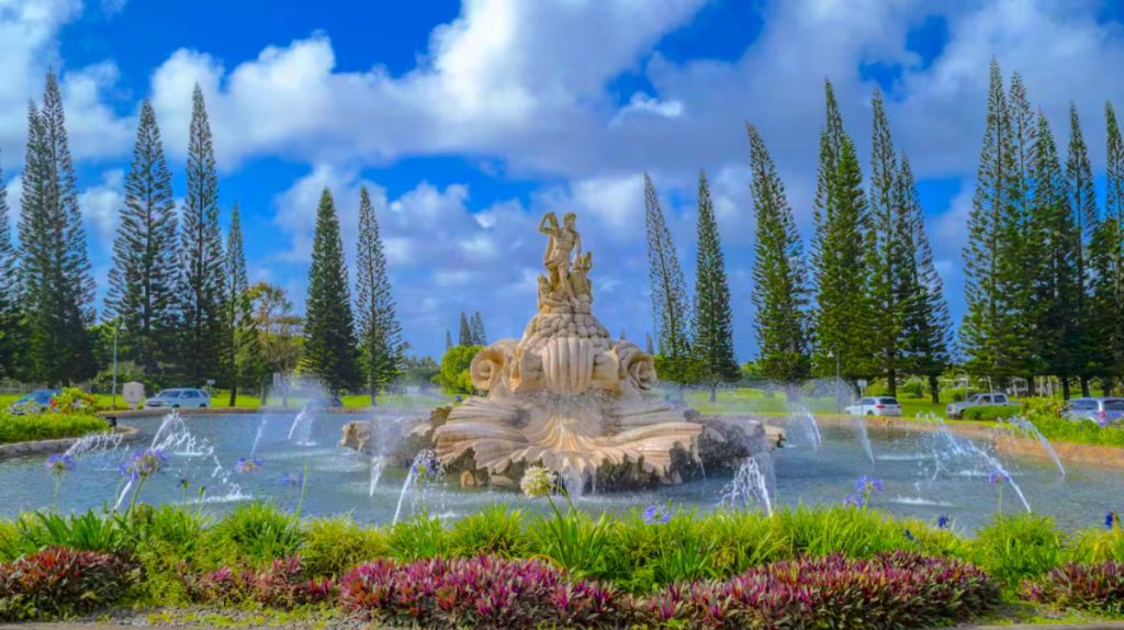 The iconic shell-shaped fountain at the entrance of Princeville, Kauai, surrounded by lush tropical greenery and towering Norfolk pines. This famous landmark is a must-see for guests staying at a Beach Kauai Vacation Rentals property on the North Shore.